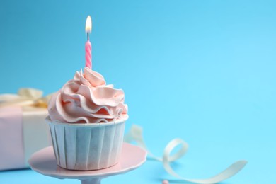 Delicious birthday cupcake with burning candle on light blue background, closeup. Space for text