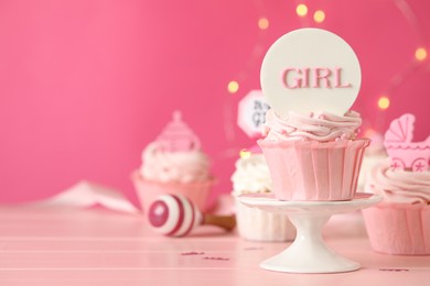 Photo of Beautifully decorated baby shower cupcakes with cream and girl toppers on pink wooden table. Space for text