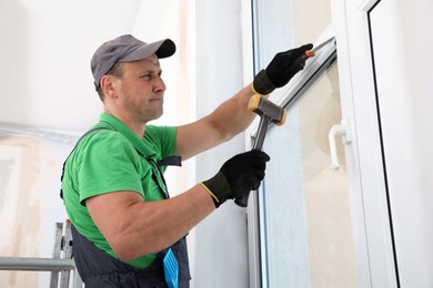 Photo of Worker in uniform installing double glazing window indoors