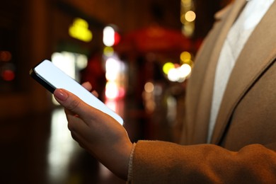 Photo of Woman with smartphone on night city street, closeup