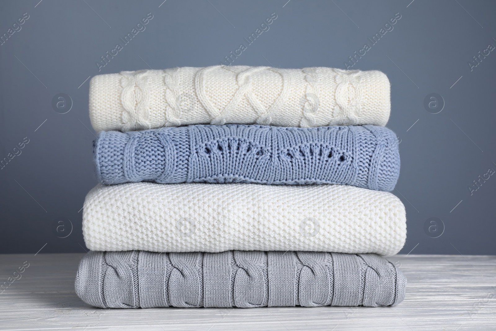 Photo of Stack of folded knitted sweaters on white wooden table against grey background