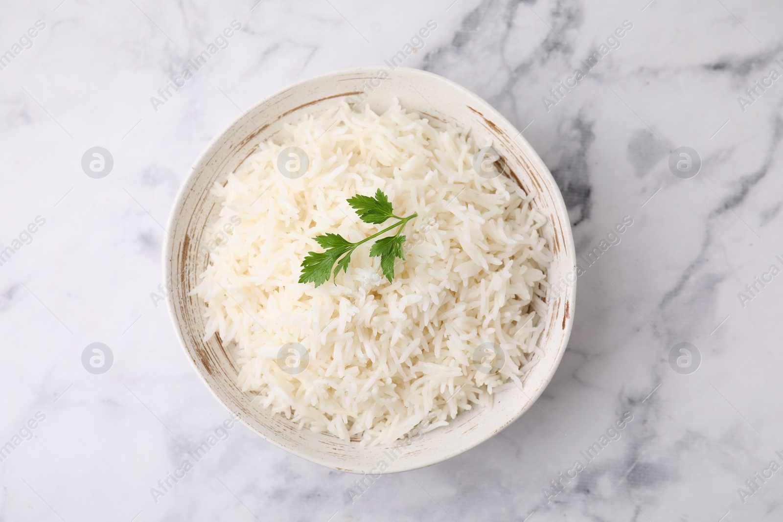 Photo of Bowl of delicious rice with parsley on white marble table, top view