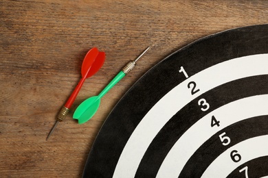 Dart board with color arrows on wooden background, top view