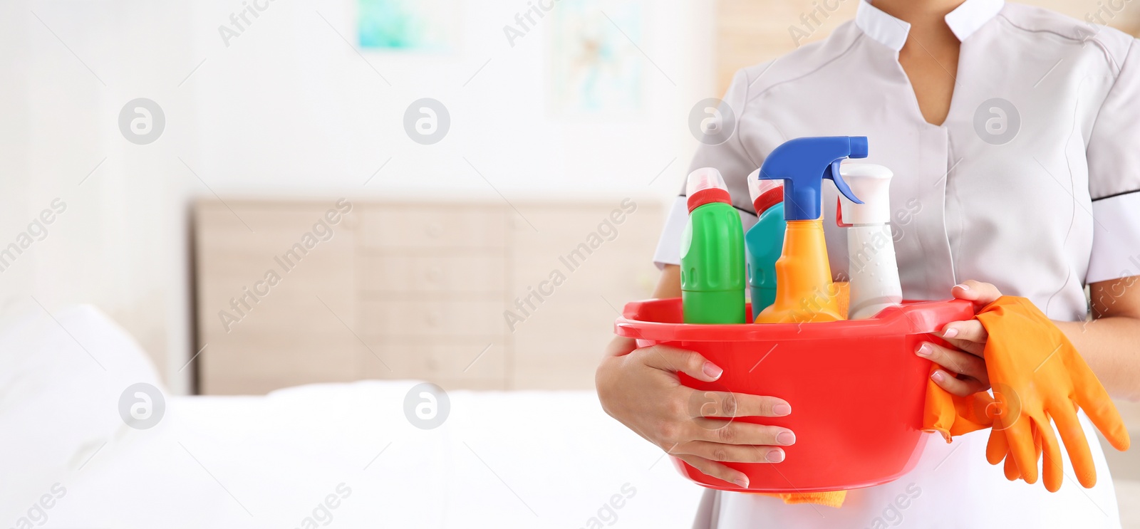 Image of Young chambermaid holding cleaning supplies in hotel room, closeup view with space for text. Banner design