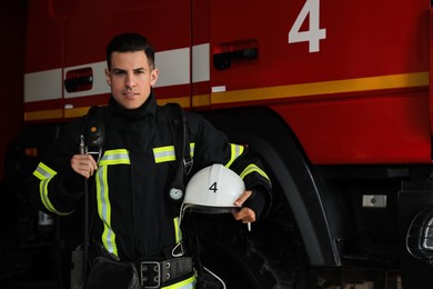 Photo of Portrait of firefighter in uniform with helmet near fire truck at station, space for text