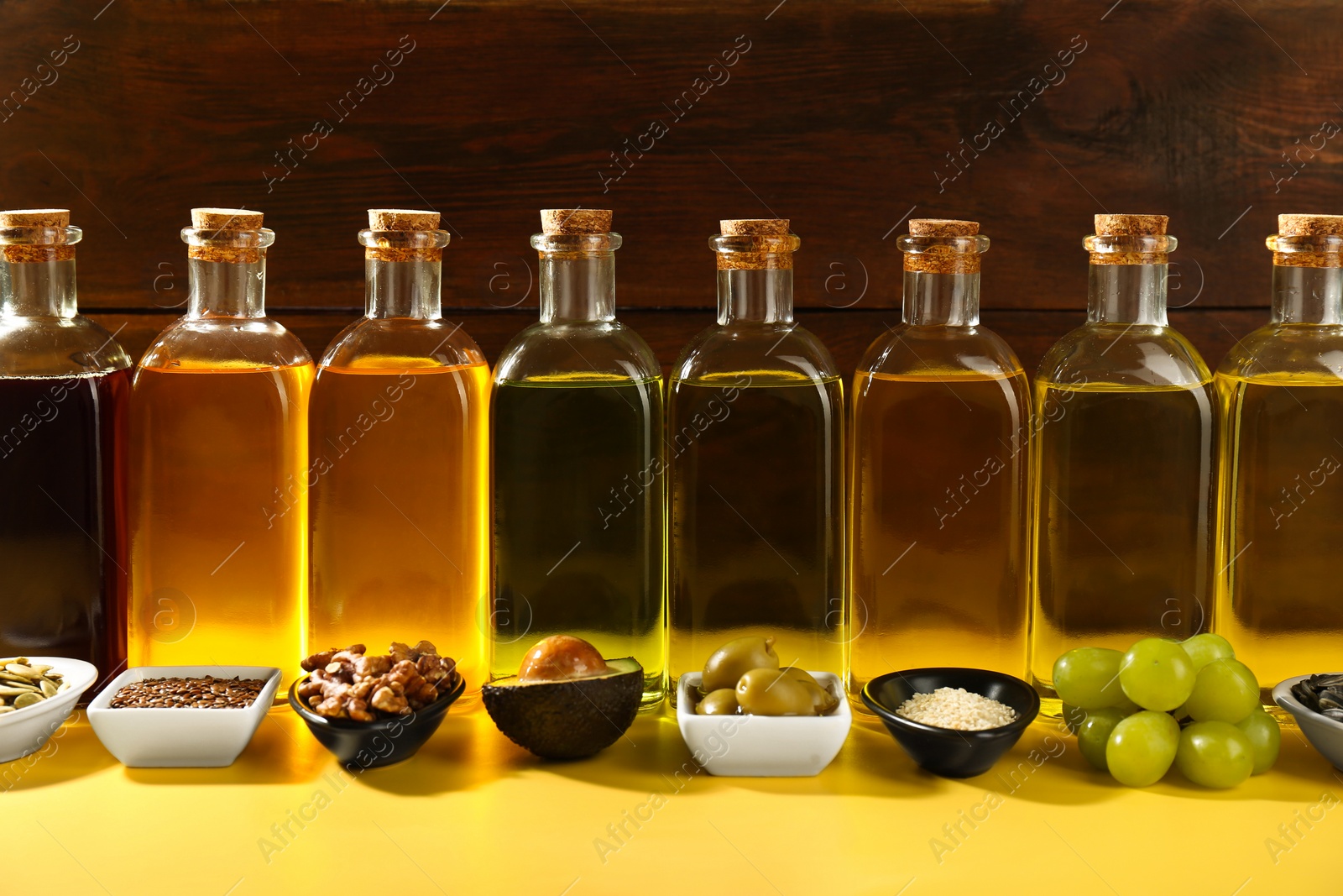 Photo of Vegetable fats. Different oils in glass bottles and ingredients on yellow table