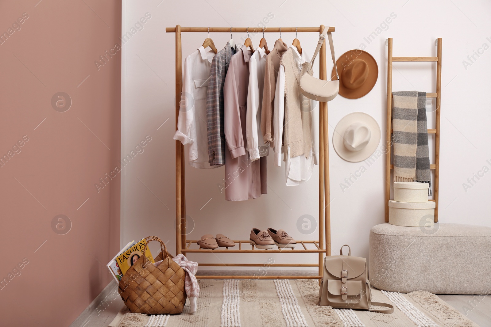 Photo of Rack with different stylish clothes and shoes near white wall in room