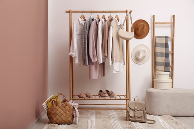Photo of Rack with different stylish clothes and shoes near white wall in room