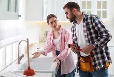 Photo of Young woman complaining to plumber about clogged sink in kitchen