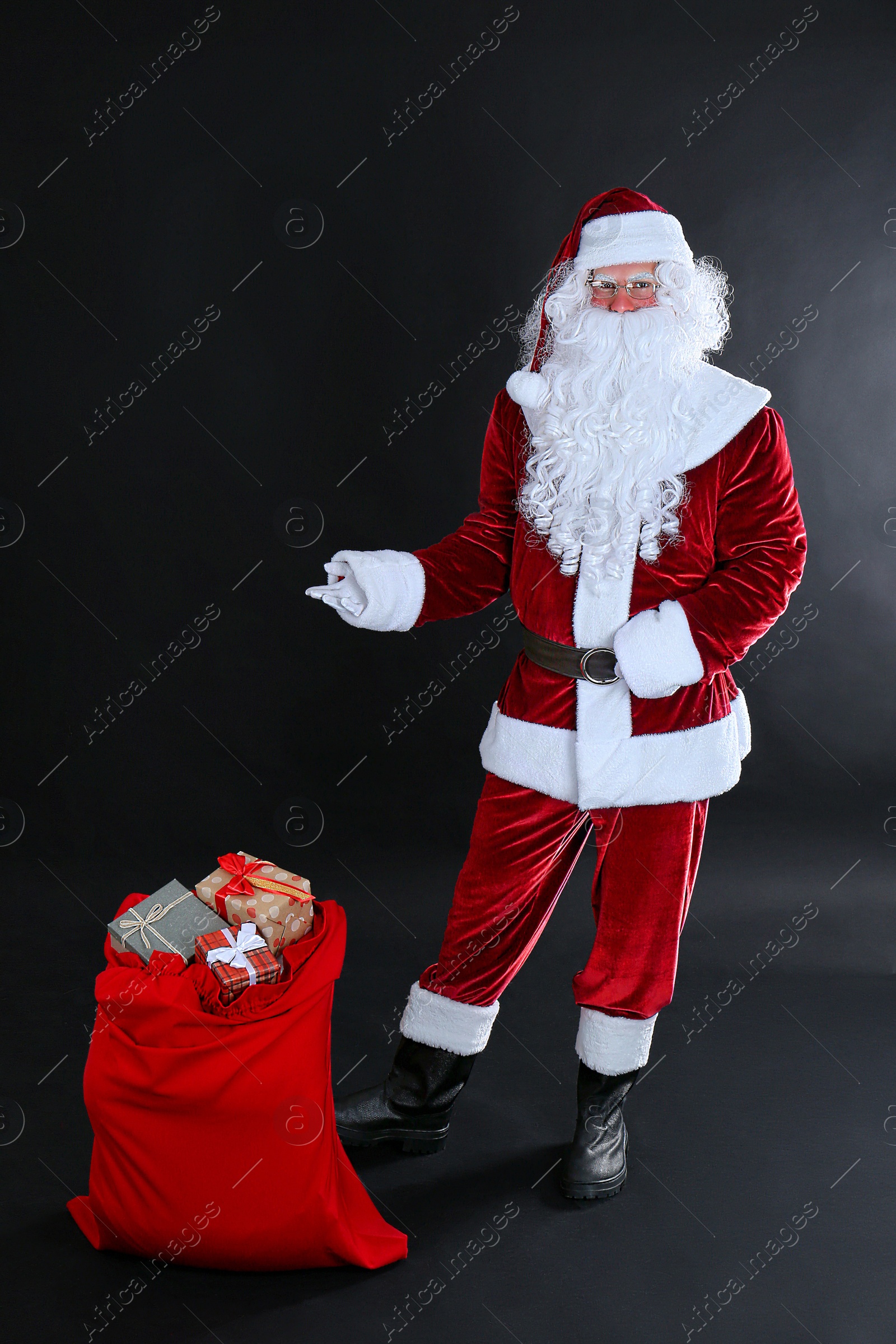 Photo of Santa Claus near sack with gift boxes on black background