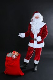 Santa Claus near sack with gift boxes on black background
