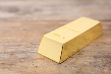 Photo of Shiny gold bar on wooden table, closeup. Space for text