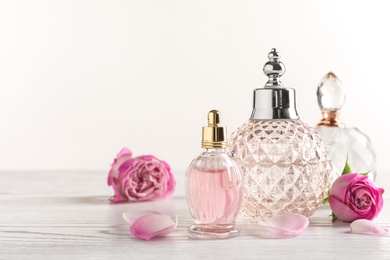 Different bottles of perfume and flowers on light background, space for text