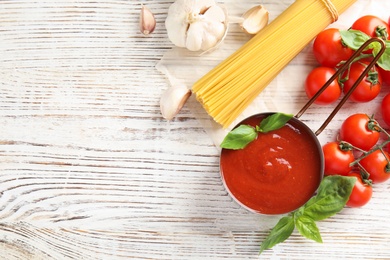 Photo of Flat lay composition with pan of sauce, pasta and tomatoes on wooden table. Space for text