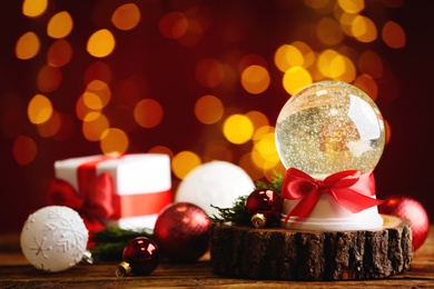 Photo of Beautiful snow globe and Christmas decor on wooden table against blurred festive lights
