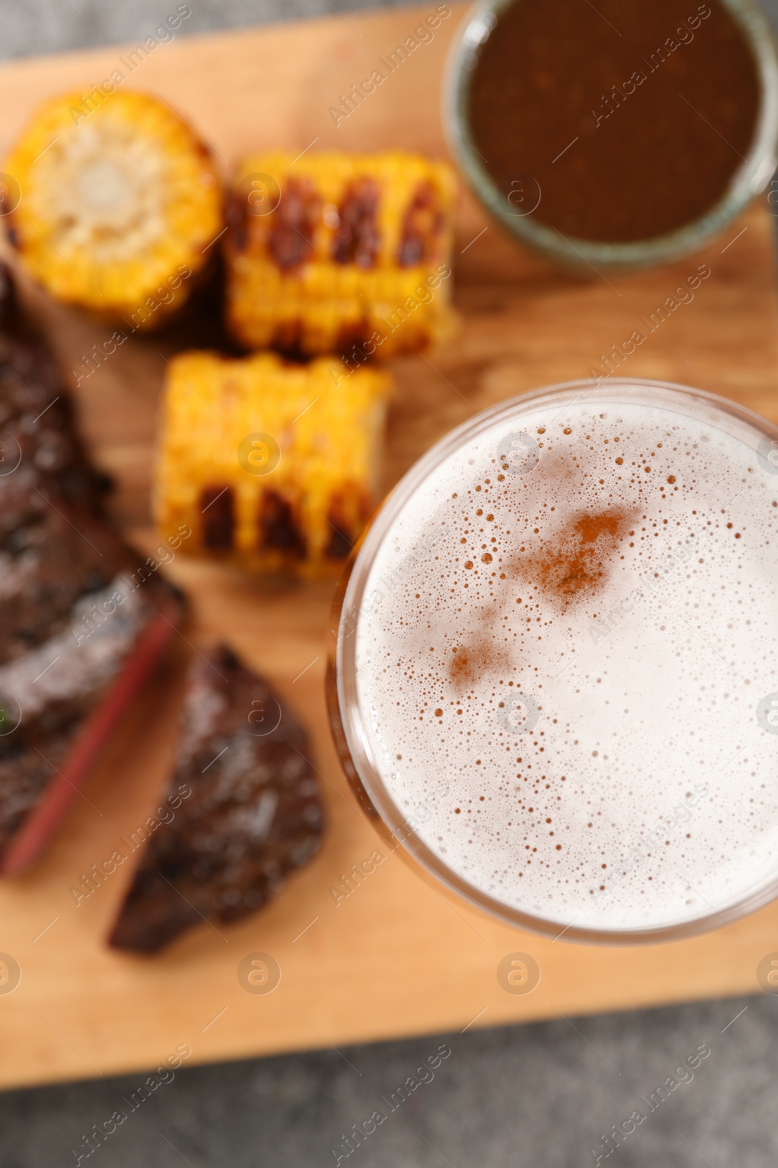 Photo of Glass of beer, delicious fried steak, corn and sauce on grey table, top view
