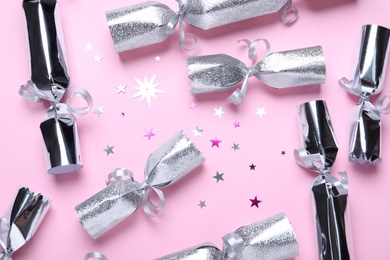 Photo of Open and closed silver Christmas crackers with shiny confetti on pink background, flat lay
