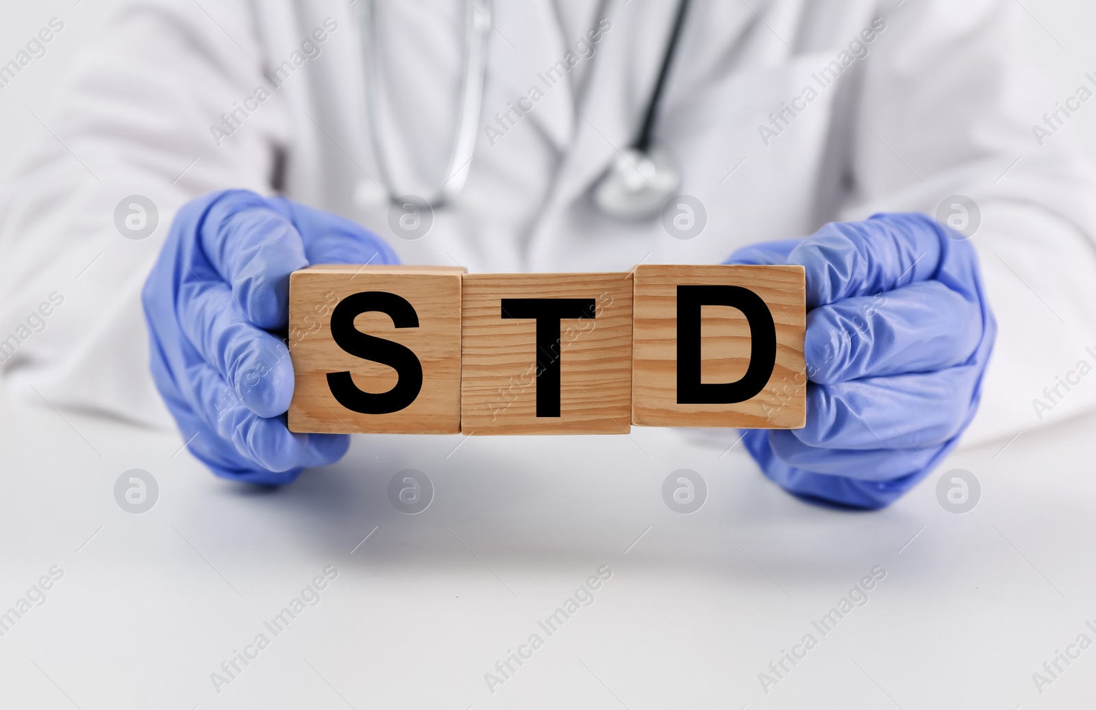 Photo of Doctor holding wooden cubes with abbreviation STD at white table, closeup