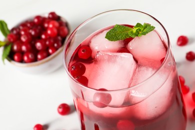 Photo of Tasty cranberry juice with ice cubes in glass and fresh berries on white wooden table, closeup