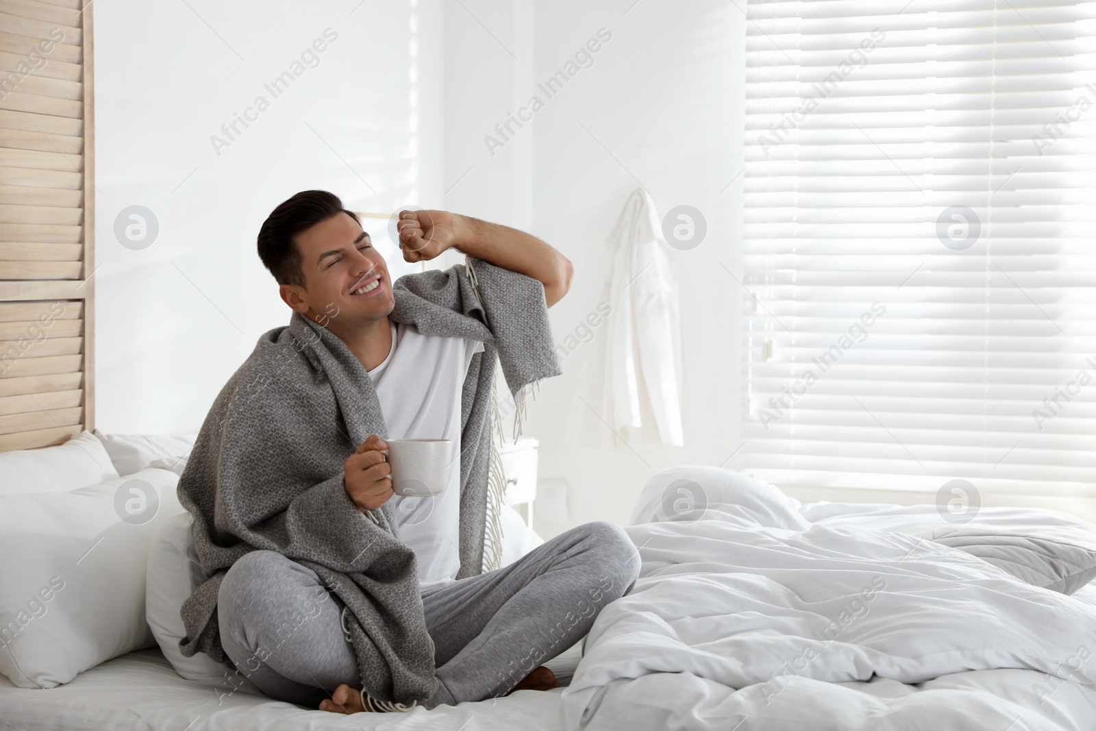 Photo of Man covered with warm grey plaid enjoying hot morning drink in bedroom