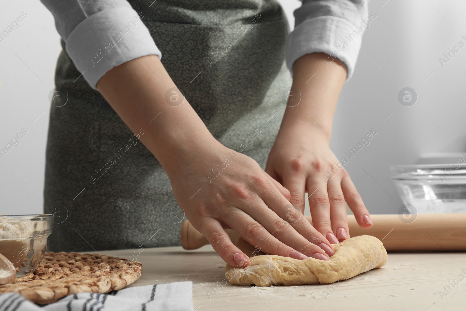 Photo of Woman kneading raw dough at white wooden table, closeup