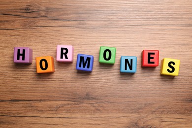Photo of Word Hormones made of colorful cubes with letters on wooden table, flat lay