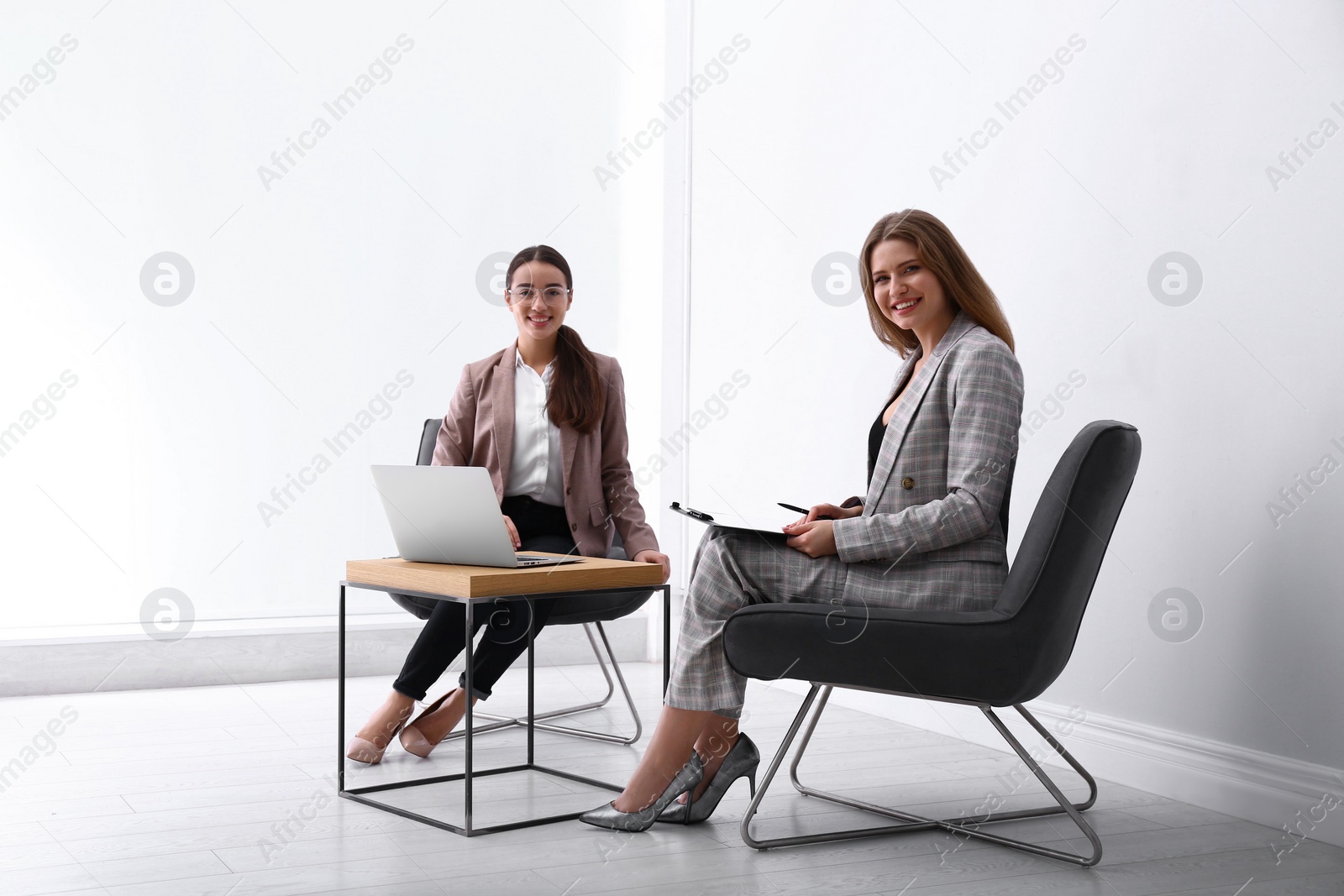Photo of Young businesswomen sitting in armchairs at table indoors