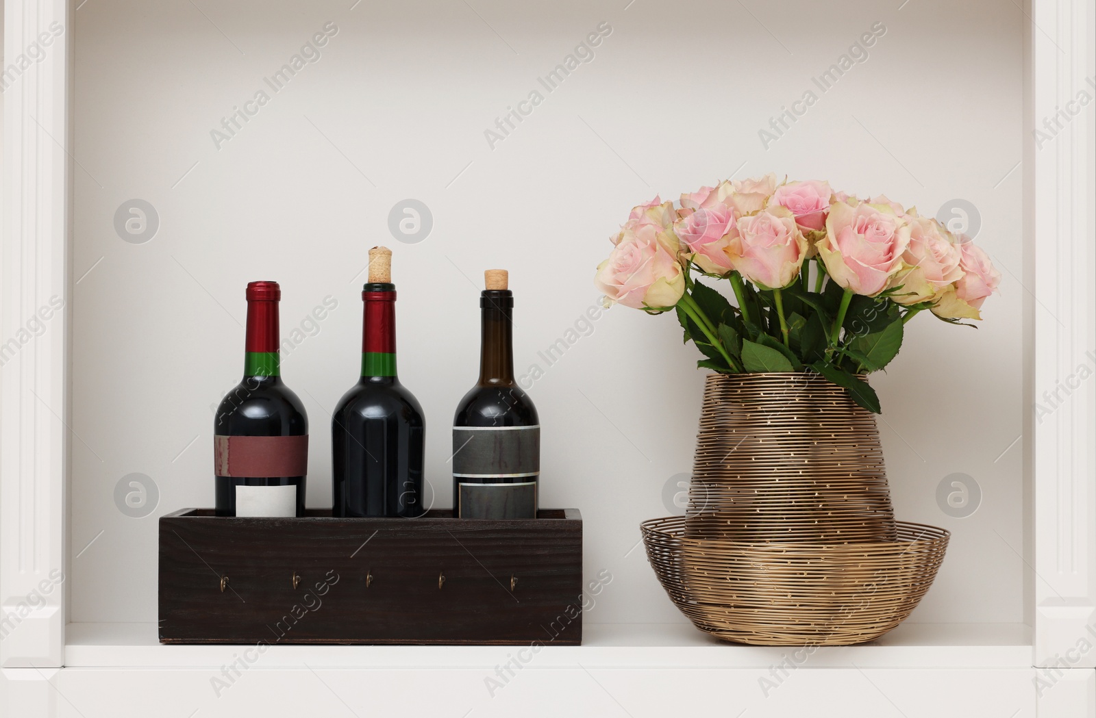 Photo of Shelf with different wine bottles and beautiful rose flowers indoors