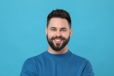 Portrait of happy young man with mustache on light blue background
