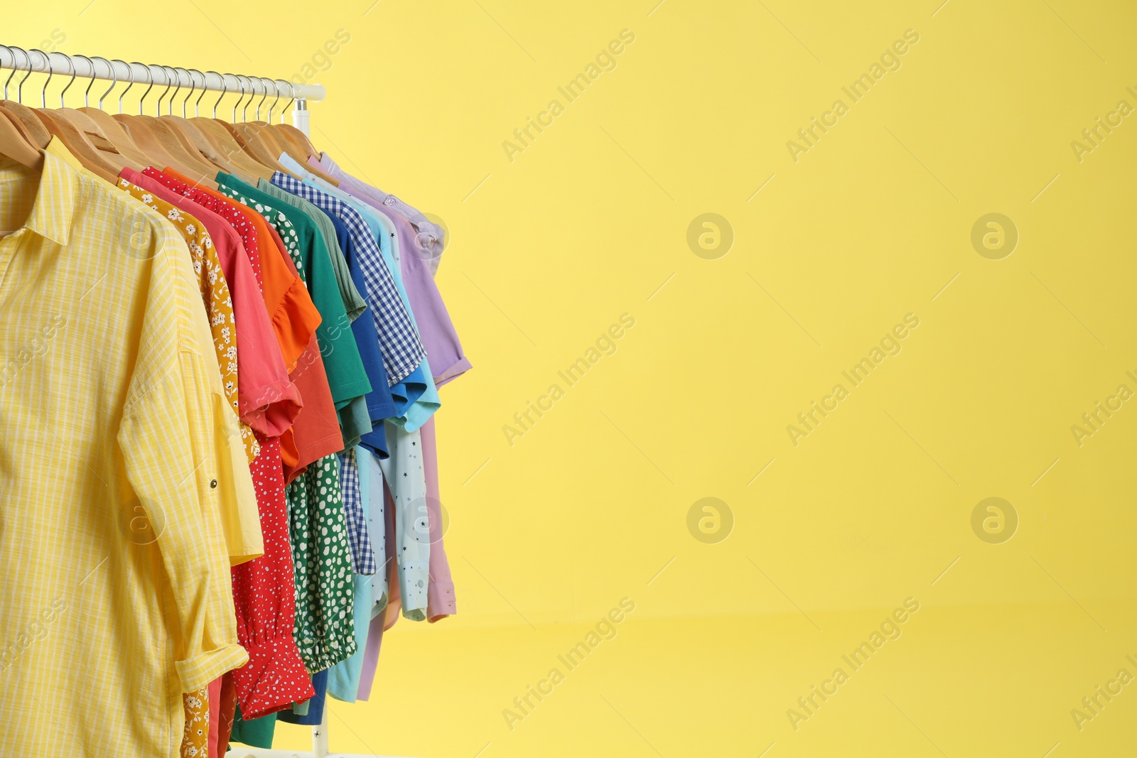 Photo of Bright clothes hanging on rack against yellow background, space for text. Rainbow colors