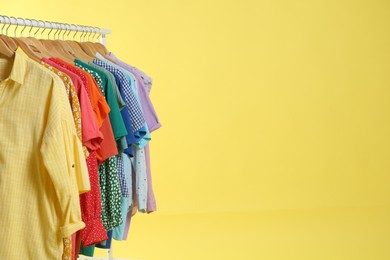 Bright clothes hanging on rack against yellow background, space for text. Rainbow colors