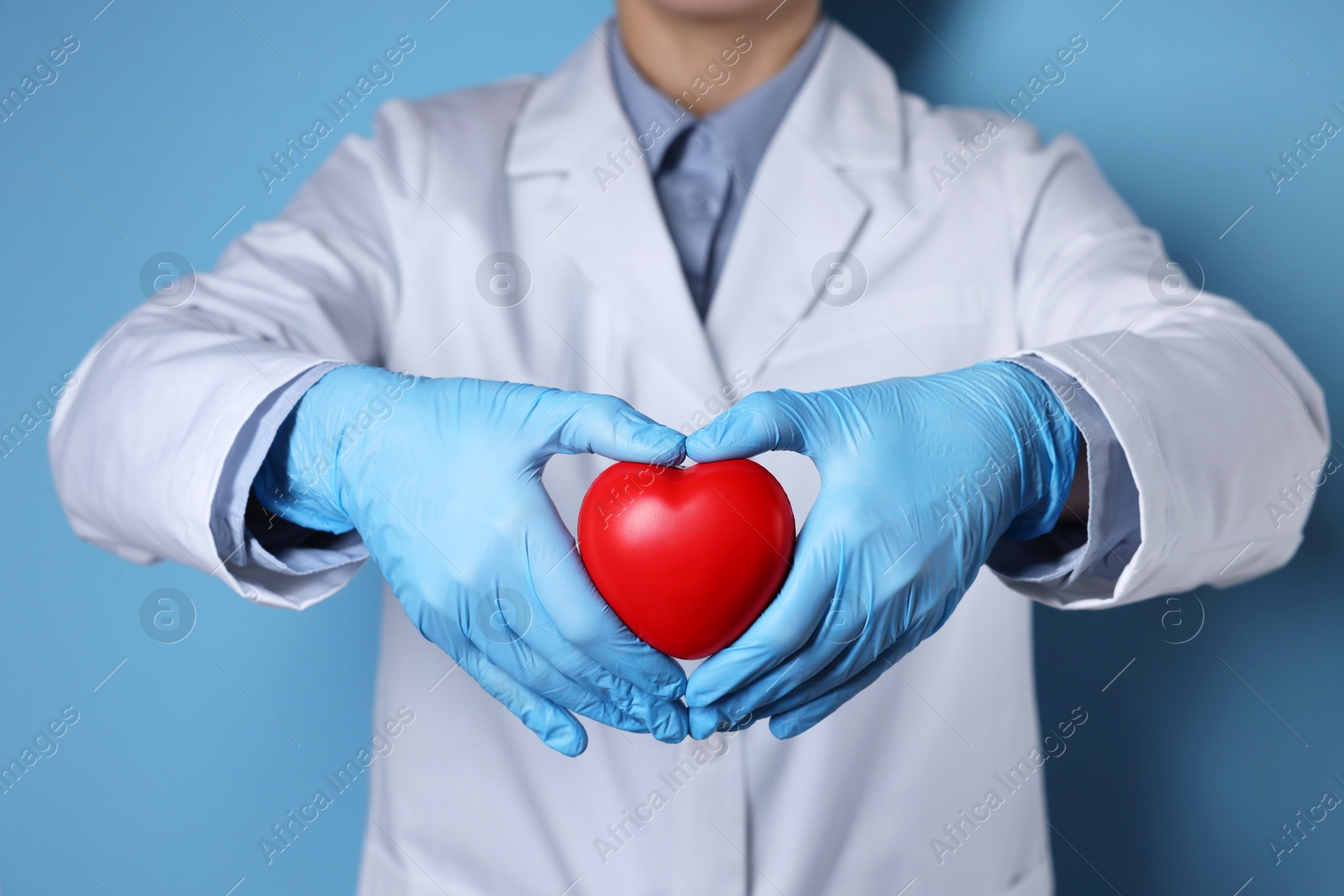 Photo of Doctor wearing medical gloves holding decorative heart on light blue background, closeup