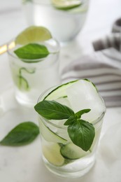 Tasty fresh cucumber water with sliced lime and basil on white table, closeup