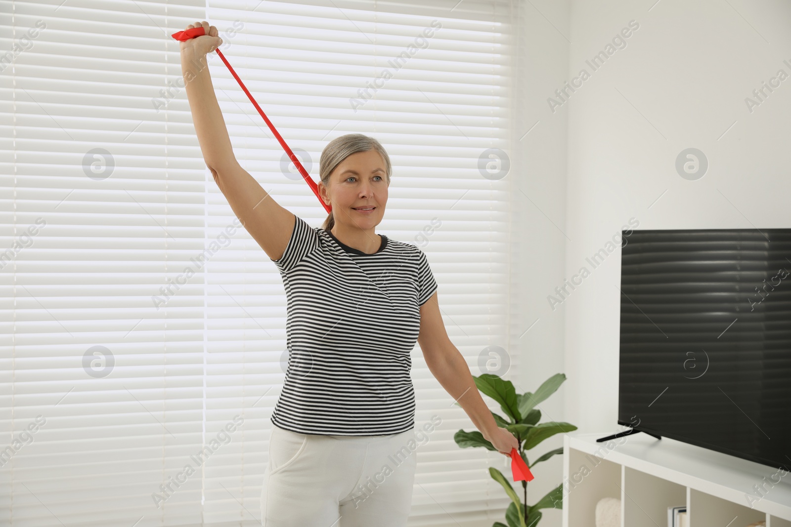 Photo of Senior woman doing exercise with fitness elastic band at home