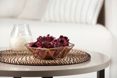 Aromatic potpourri of dried flowers in bowl and candle on white table indoors