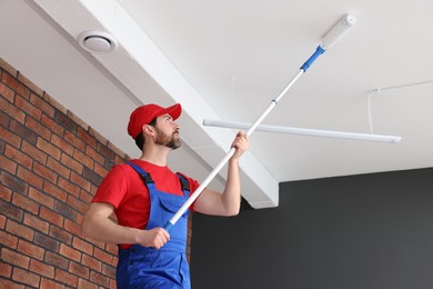 Photo of Handyman painting ceiling with roller in room