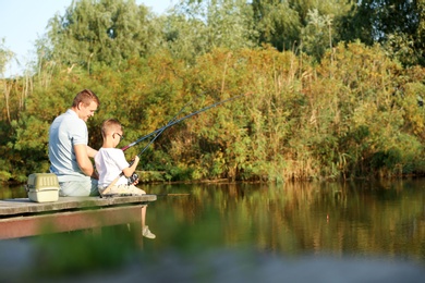 Photo of Dad and son fishing together on sunny day. Space for text