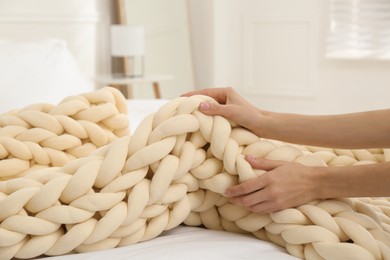 Woman folding chunky knit blanket at home, closeup