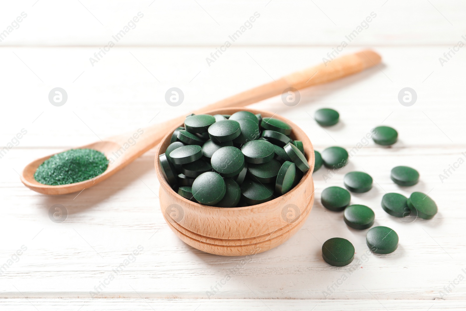 Photo of Bowl of spirulina pills and powder in spoon on wooden background