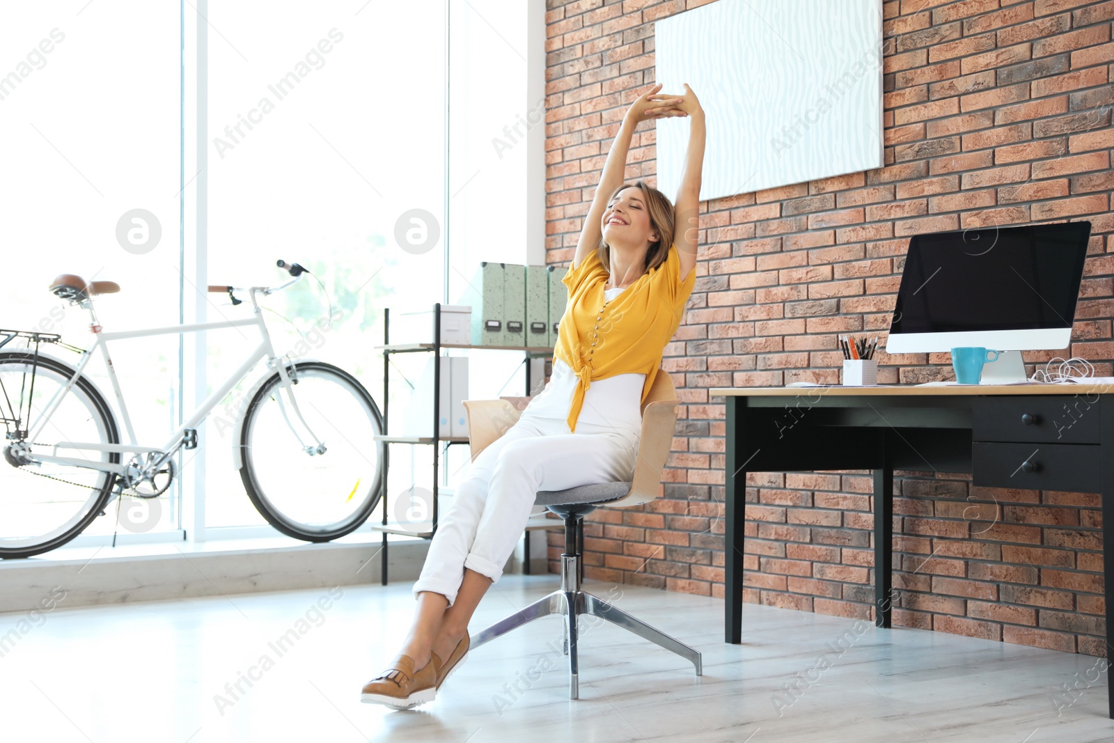 Photo of Beautiful young businesswoman stretching in office. Workplace fitness