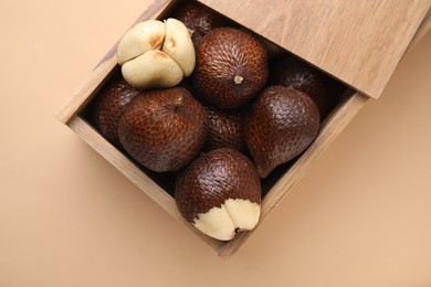 Photo of Wooden crate with fresh salak fruits on beige background, top view