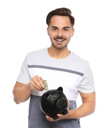 Photo of Portrait of young man putting money into piggy bank on white background