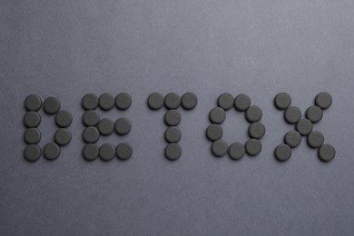 Photo of Word Detox made with activated charcoal pills on dark background, flat lay. Natural sorbent
