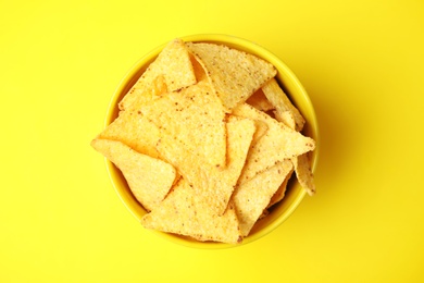 Photo of Bowl of tasty Mexican nachos chips on yellow background, top view