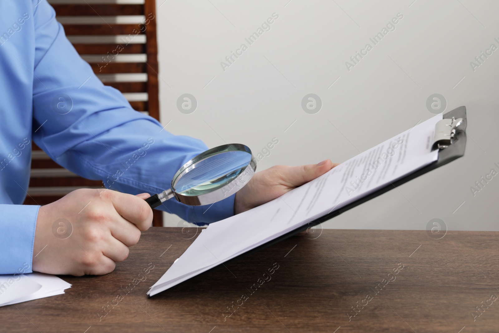 Photo of Man looking at document through magnifier at wooden table, closeup. Searching concept