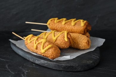 Photo of Delicious deep fried corn dogs with mustard on black table