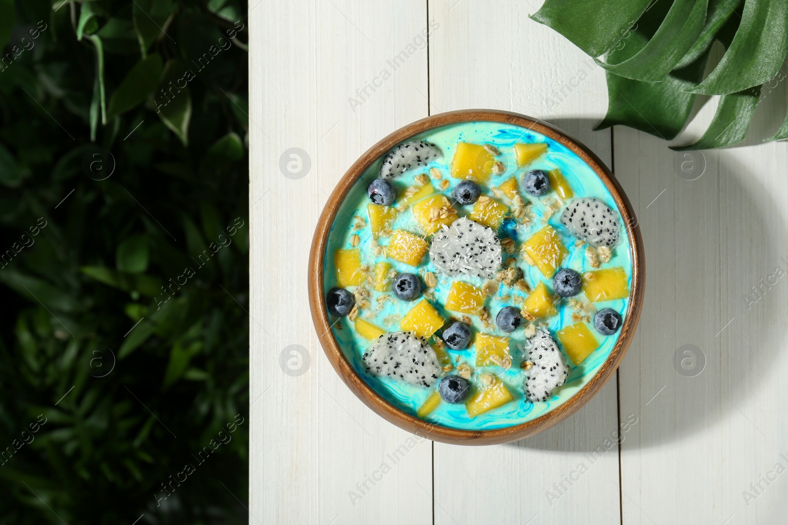 Photo of Delicious smoothie bowl with fresh fruits, blueberries and oatmeal on white wooden table outdoors, top view. Space for text