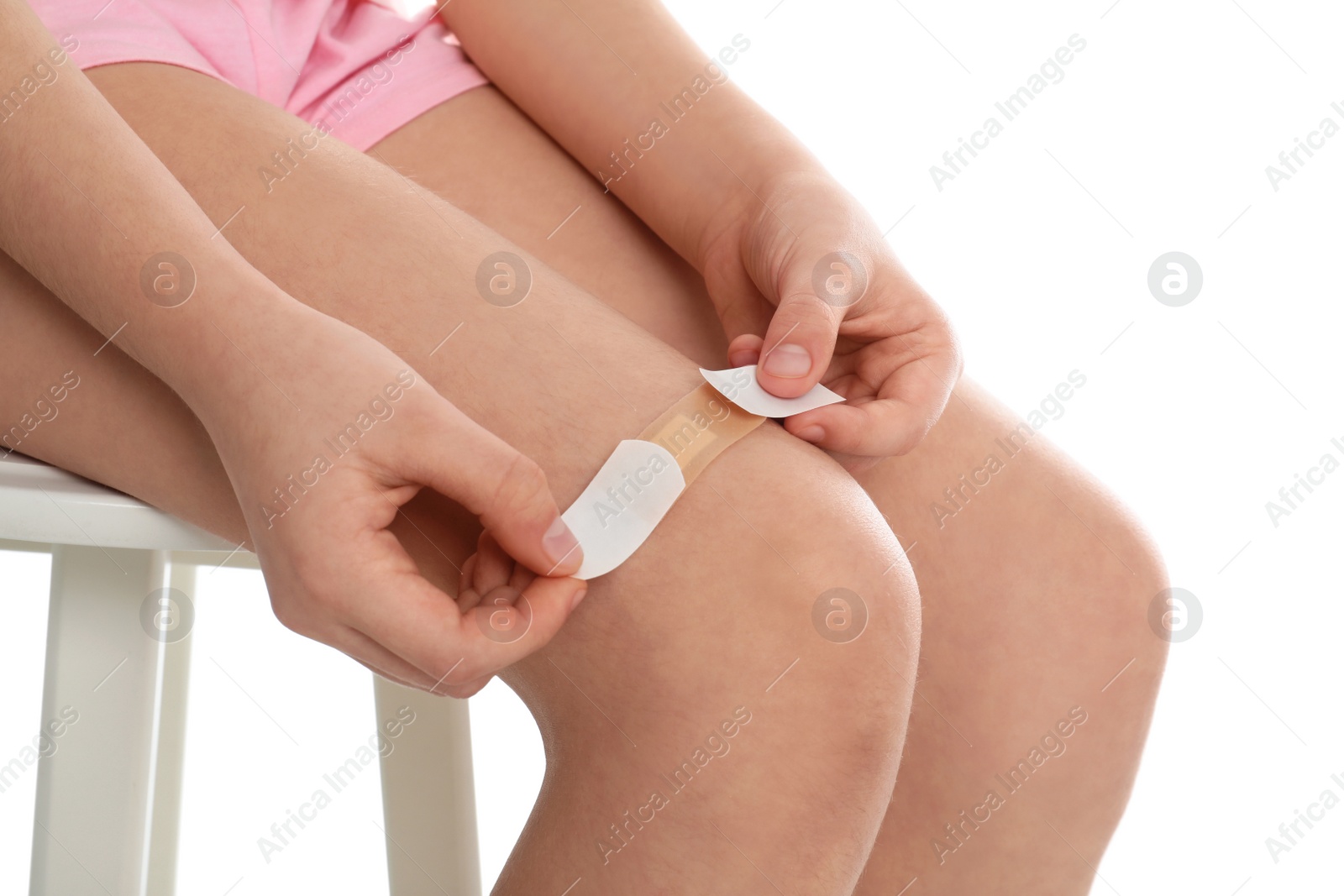 Photo of Girl putting sticking plaster onto leg on white background, closeup