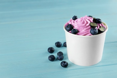 Photo of Cup with tasty frozen yogurt and blueberries on blue wooden table. Space for text