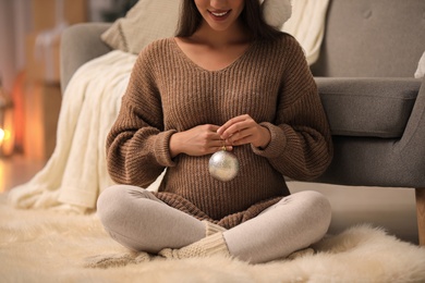 Photo of Happy pregnant woman with Christmas ball at home, closeup. Expecting baby